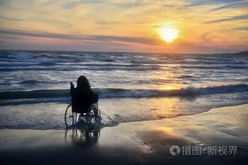 日落,使观光在海滩上,一个坐在轮椅上的女人