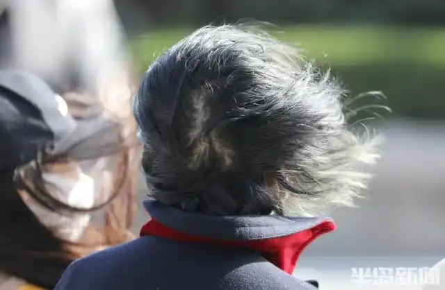 的大风让路上的行人走路有些吃力,有的市民头上戴的帽子险些被风吹走