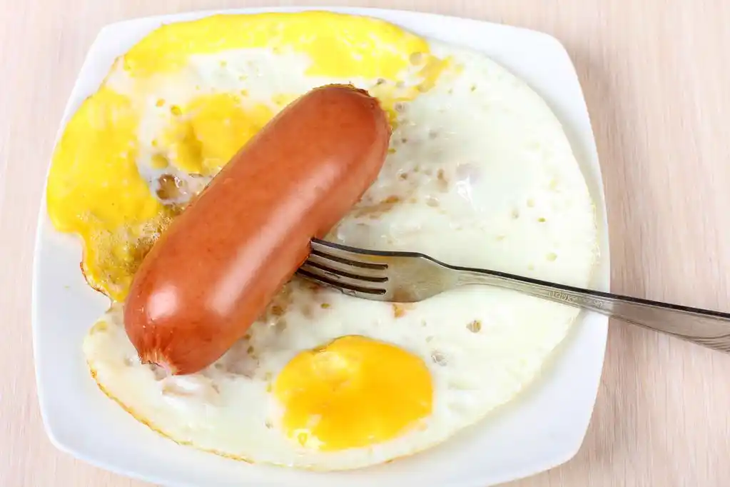 煎的鸡蛋和叉,煎的鸡蛋和香肠在白色瓷碟上